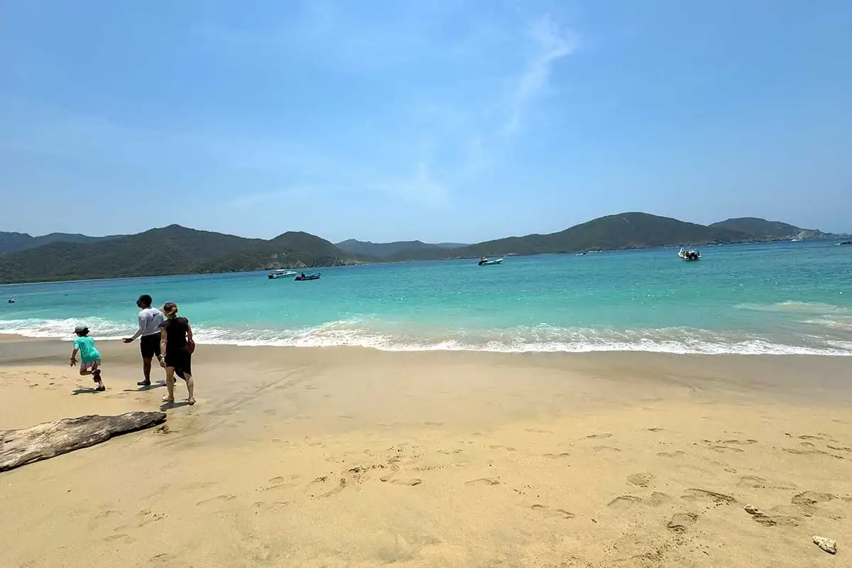Familia caminando por la arena vacía de Playa Cinto, con lanchas fondeadas en la bahía